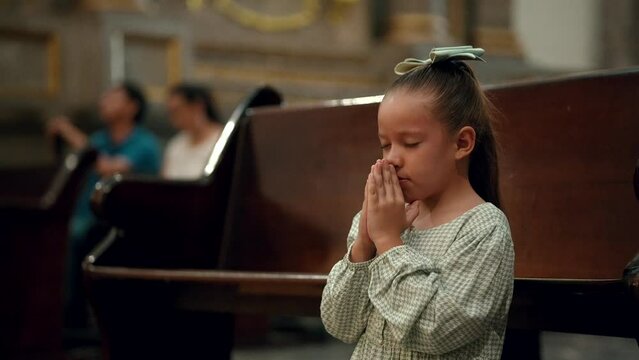 Ni&ntilde;a hermosa rubia latina hispana rezando meditando orando con sus manos juntas hincada de rodillas pidiendo en el templo iglesia parroquia bas&iacute;lica santuario 