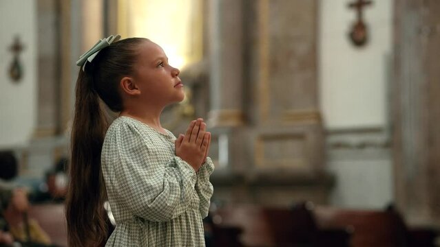 Ni&ntilde;a hermosa rubia latina hispana rezando meditando orando con sus manos juntas hincada de rodillas pidiendo en el templo iglesia parroquia bas&iacute;lica santuario con su mirada a Dios