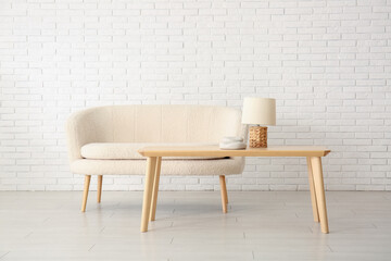 Cozy white sofa, table and lamp near brick wall