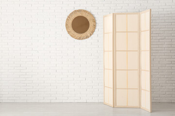 Folding screen and mirror near white brick wall