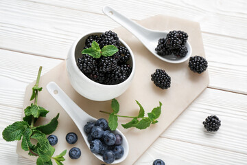 Bowl with fresh blackberry and blueberry on light wooden background, closeup
