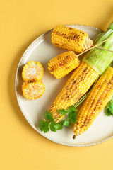 Plate with tasty grilled corn cobs and parsley on yellow background