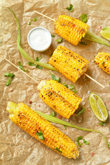 Baking paper with tasty grilled corn cob skewers and sauce, closeup