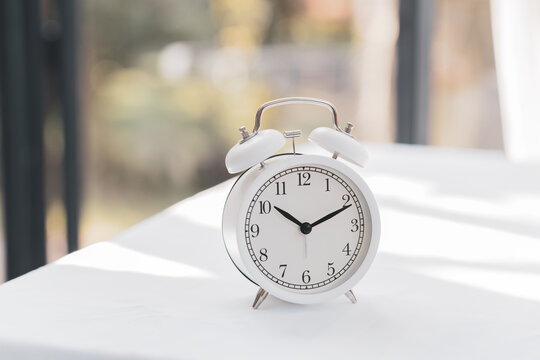 Alarm clock on white wooden table with copy space blurred background. Beauty concept with beautiful spa composition set.