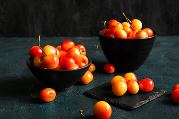 Fototapeta na wymiar Bowls with sweet yellow cherries on dark background