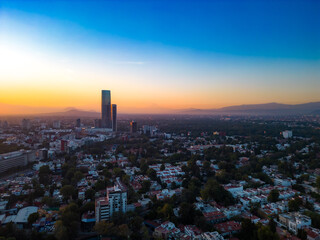 Aerial view of amazing sunrise over modern city with skyscraper of Mexico City with tall Mitikah Tower at bright orange sunrise with blue sky over foggy mountains in morning time