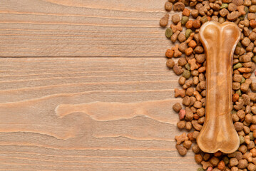 Heap of dry dog food and chew bone on wooden background