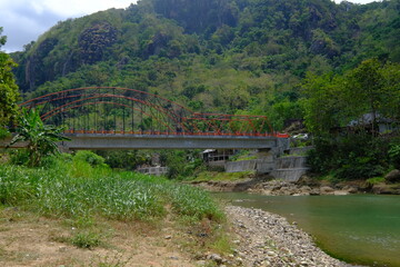 Obraz premium steel bridge over rocky river. tropical green mountains.