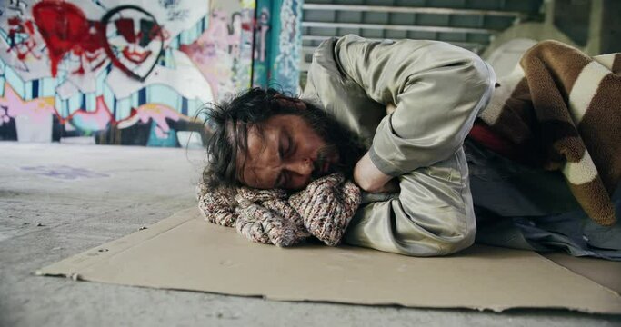 Homeless man sleeping under a bridge laying on a piece of cardboard