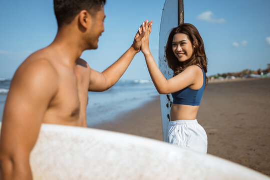 couple holding a surfboard and giving a high five to each other on a blue sky beach