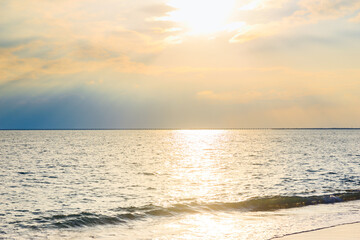 On a clear summer day, the sunset sun shines through the clouds and onto the sea