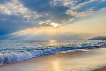 Sunset on the Sanya beach, the sun shines through the clouds on the golden sea and beach