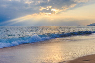 Sunset on the Sanya beach, the sun shines through the clouds on the golden sea and beach