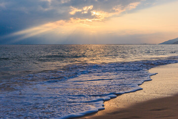 Sunset on the Sanya beach, the sun shines through the clouds on the golden sea and beach