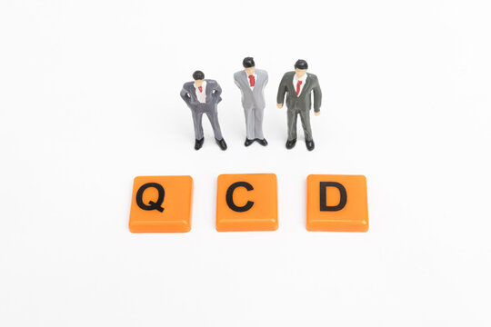 Three miniature businessman look at the QCD word. QCD print screen on orange plate. The concept of Quality, Cost, Delivery. The concept of QCD Analysis. business and Strategy concept.
