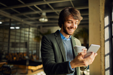 Young man having a coffee break and using his smart phone while working in a startup company