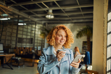 Young woman using a smart phone while looking through the window in a startup company office