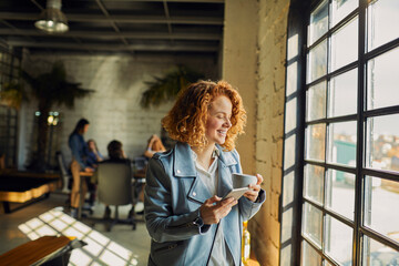 Young woman using a smart phone while looking through the window in a startup company office