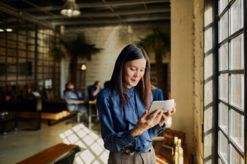 Young woman using a smart phone while looking through the window in the office