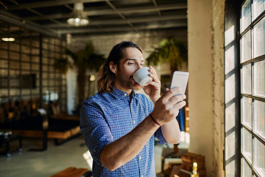 Young man having a coffee break and using his smart phone while working in a startup company