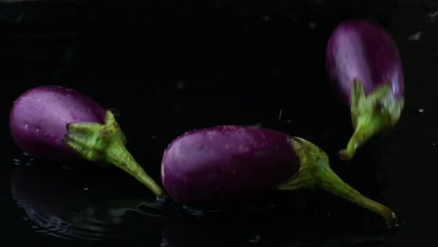 Purple eggplants being tossed and tumbling through water on black background. 