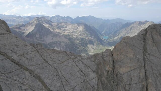 Drone footage passing by a crest and revealing a green valley behind the Vignemale in the Pyrenees mountains.