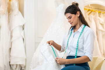 Obraz premium Portrait of entrepreneur bridal shop owner business woman fashion designer stylish working.Attractive designer girl using tape meter fitting on wedding dress with mannequin at wedding studio