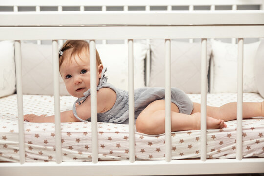 Happy little 9 month old girl lying on her stomach in her crib. Children's furniture, children's textiles. High quality photo