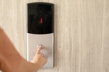 A woman presses her finger on the up button of an elevator in the building. In the present, the elevator screen shows the 1st floor and the woman presses the up button to go to the top.