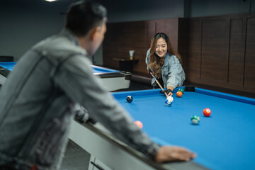 female pool player poking the white ball while the male player standing at the side of the pool