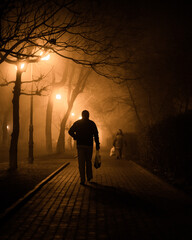 Solitary figure walks along foggy street, dawn breaking, spooky atmosphere.