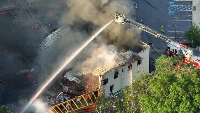 Firefighter on ladder spraying with water on burning building after explosion in american city - Aerial top down