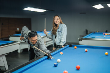 male pool player poking the white ball with the female player standing behind while playing...