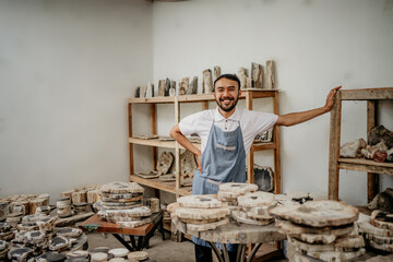 smiling male entrepreneur wearing an apron with his hands on his waist standing in a stone craft warehouse