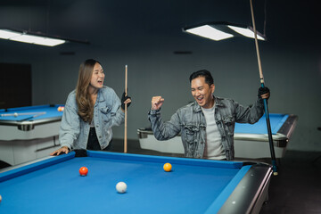 Fototapeta premium excited male pool player celched his arm and screming happily while playing biliard game with his partner at billiard studio
