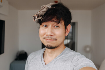 Close up of happy asian man with his Sugar Glider pet climbing around his head.