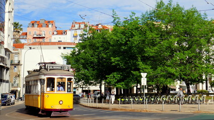 Plakat gelbe nostalgische Straßenbahn in Lissabon fährt neben grünen Bäumen bei Sonne durchs Zentrum