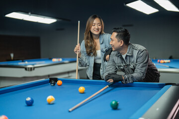 Fototapeta premium asian woman holding the cue stick while standing put her hand on the shoulder of her friends during the break