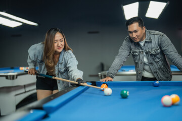 female pool player poking the white ball with the female player standing next to her
