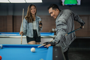 excited male pool player smiling while poking the cue ball from his back at the billiard game