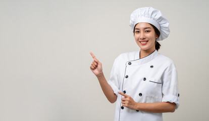 Smiling Young beautiful asian woman chef in uniform pointing finger to copy space isolated background. Cooking woman Occupation chef or baker People in kitchen restaurant and hotel.