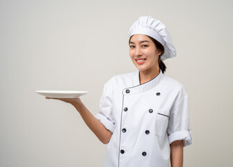 Smiling Young beautiful asian woman chef in uniform holding empty plate delicious dish menu good taste on isolated. Cooking woman Occupation chef or baker People in kitchen restaurant and hotel.