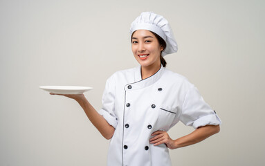 Smiling Young beautiful asian woman chef in uniform holding empty plate delicious dish menu good taste on isolated. Cooking woman Occupation chef or baker People in kitchen restaurant and hotel.
