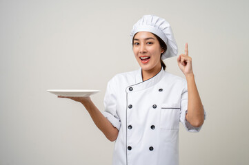 Smiling Young beautiful asian woman chef in uniform holding empty plate delicious dish menu good taste on isolated. Cooking woman Occupation chef or baker People in kitchen restaurant and hotel.