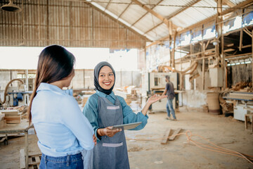 veiled female waitress serving a female customer while holding a tablet in a woodcraft workshop