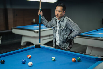 Fototapeta premium portrait of confuse pool player put his hand on his waist while observing the billiard balls