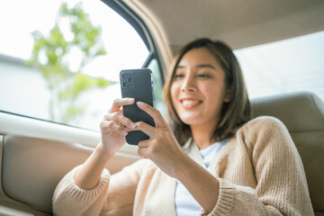 Relaxing moment of beautiful woman sitting in car back seats using smartphone play social media...