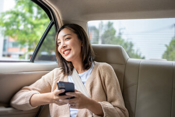 Relaxing moment of beautiful woman sitting in car back seats using smartphone play social media with safety belt and look out the window. Female happy in car traveling on the road to destination.