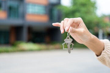 Woman buying or rent new home she holding key front of new house. Surprise happy young asian woman giving house key and smile to rent or purchase apartment home. Moving relocation concept.