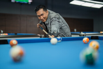 male billiard player aiming the ball seriously using the cue stick while playing billiard at the billiard studio